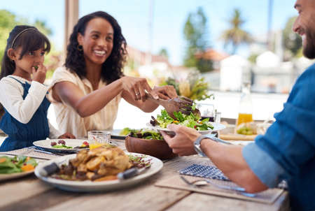 She always makes sure we maintain a healthy diet. a beautiful young woman dishing up salad on her husbands plate while enjoying a meal with family outdoors.の写真素材