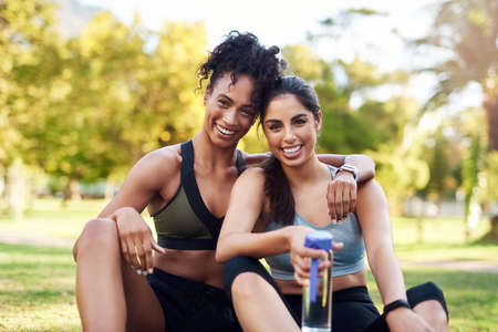 Proud of my friend. Cropped portrait of two attractive young women sitting close to each other and smiling while in the park.の写真素材