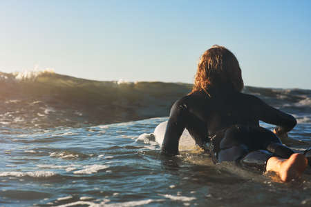 This is what I call rising to the occasion. Rearview shot of a young man surfing in the ocean.の写真素材
