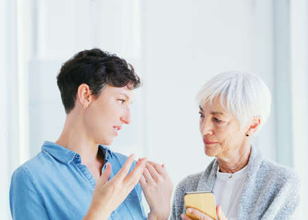 This is how social media works. a senior woman holding a cellphone while talking with her attractive young daughter while at home.の写真素材