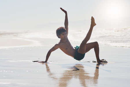 I am passionate about my dancing. Full length shot of a handsome young man performing a challenging dance sequence on the beach during the day.の写真素材