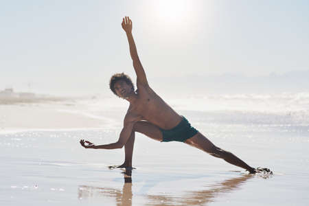 Dancing is my art. Full length shot of a handsome young man dancing shirtless on the beach during the day.の写真素材