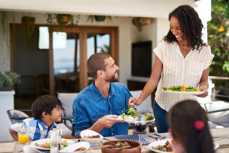 Were living on the green side of life. a beautiful young woman dishing up salad on her husbands plate while enjoying a meal with family outdoors.の写真素材