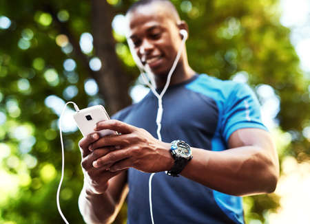 This is what I call connection on the go. a handsome young man listening to music and using his cellphone while exercising outdoors in the city.の写真素材