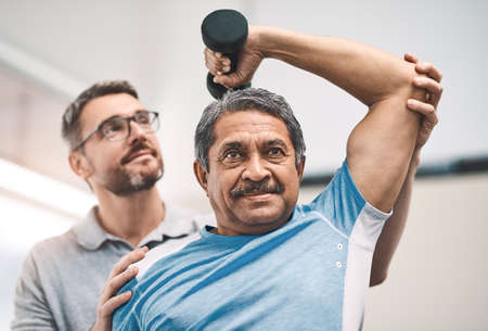 Hes getting stronger by the day. a senior man exercising with dumbbells during a rehabilitation session with his physiotherapist.の写真素材