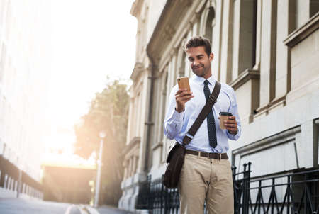Who could be messaging me now. a handsome young businessman texting on his cellphone while heading to work in the morning.の写真素材