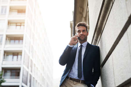 Taking a bit of time before going to work. Portrait of a handsome young businessman talking on his cellphone while heading to work in the morning.の写真素材