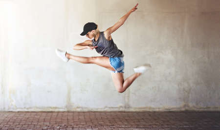 Jumping to new heights in dance. Full length shot of an attractive young woman jumping and doing a half split as part of a dance routine.の写真素材
