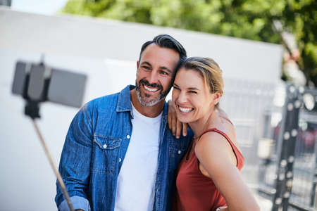 Hashtag cant get enough of each other. an affectionate couple taking a selfie together with a selfie stick outdoors.の写真素材