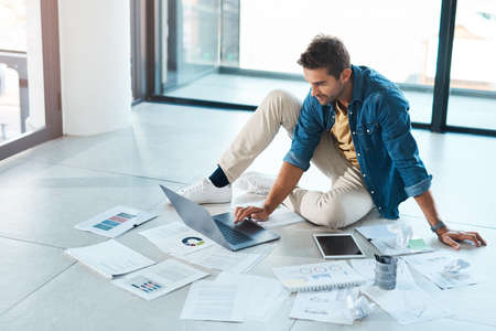 Planning is everything when it comes to success. a young businessman brainstorming with a laptop and paperwork on a floor in an office.の写真素材