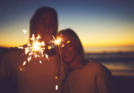 Light up the night with some magic. a young couple playing with sparklers on the beach at night.の写真素材