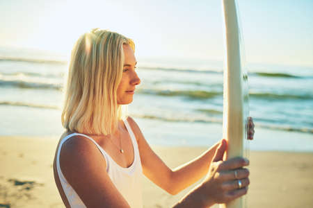 Surfing is a lifestyle. an attractive young woman standing in a swimsuit holding a surfboard on the beach.の写真素材