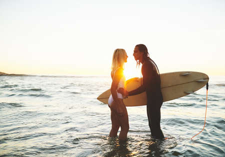 You and the sea complete me. an affectionate young couple with a surfboard kissing on the beach at sunset.の写真素材