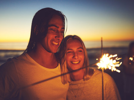 The spark between us will never fade away. a young couple playing with sparklers on the beach at night.の写真素材