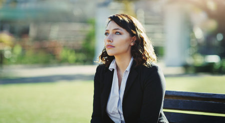 Some time at the park can make you feel better. an attractive young businesswoman feeling depressed while sitting in a public park.の写真素材
