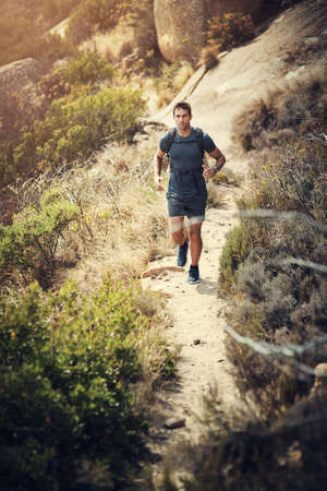 Hiking is good for the body and mind. Full length shot of a handsome young man running during his hike in the mountains.の写真素材