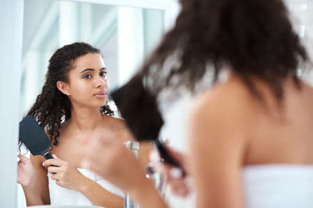Good days start with good hair. a beautiful young woman brushing her hair in the bathroom at home.