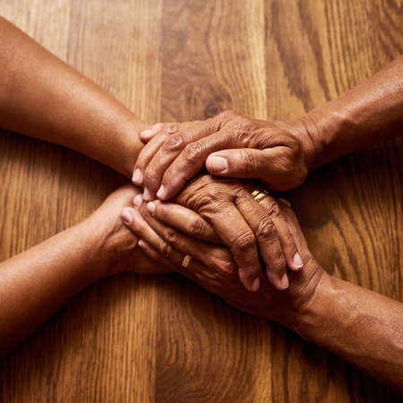 Together we handle anything thrown our way. High angle shot of an unrecognizable senior couple holding hands together over a wooden table at home.の写真素材