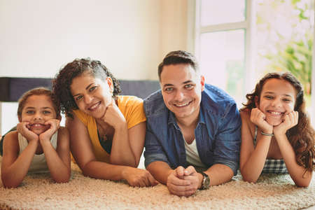 My family is my everything. Portrait of a family of four smiling at the camera while lying on the floor.の写真素材