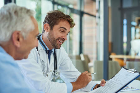 The results show that hes in excellent health. a handsome doctor going over some paperwork with a male senior patient in a clinic.の写真素材
