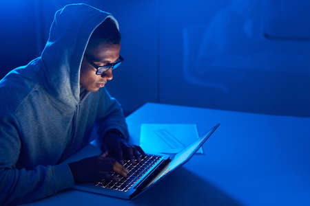 Keeping tabs of all your online activity. a young male hacker using a laptop in the dark.の写真素材