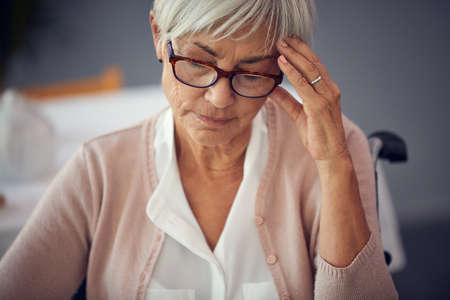 I really cant handle this pain. a senior woman suffering with a headache while sitting in her wheelchair in a retirement home.の写真素材