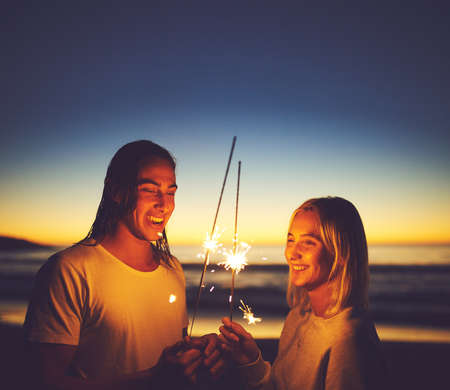 Keep the spark alive. a young couple playing with sparklers on the beach at night.の写真素材