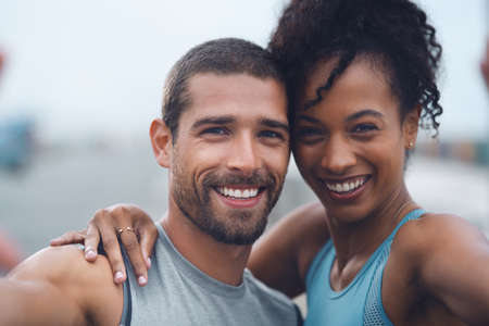 These fitness fanatics love taking selfies. Portrait of a sporty young couple taking selfies together while exercising outdoors.の写真素材
