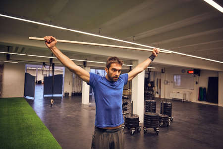 I will have the muscles I want. a handsome young man working out with a stick in the gym.