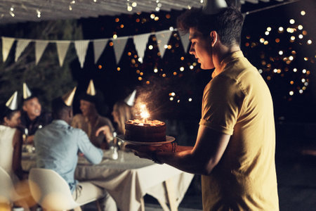 Trying my best to not drop the birthday cake. a handsome young man carrying a cake at a birthday celebration with friends outdoors in the evening.の写真素材