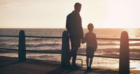 enjoying the view with my little man. Rearview shot of a father and son watching the sun set at the beach.の写真素材