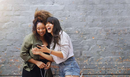 Social media always has us laughing out loud. two cheerful young women using a cellphone together...