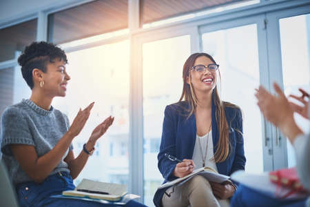 This is what you call a productive environment. a group of young businesswomen giving their colleague a round of applause during a meeting at work.の写真素材