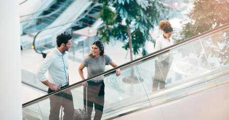 On the way to take a chance at success. two young businesspeople having a chat while going up an escalator in a modern workplace.の写真素材