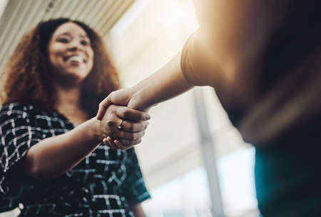I know well do great together. Low angle shot of an attractive young businesswoman shaking hands with an associate in a modern workplace.の写真素材