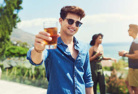 I hope everyone is enjoying their holidays as well. Portrait of a handsome young man raising up his glass for a toast while relaxing outdoors with his friends.の写真素材