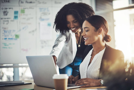 Technology pushes them to achieve more. two businesswomen working together on a laptop in an office.の写真素材