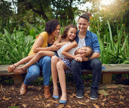 Priceless family moments. Full length shot of a happy family spending some time together on a bench at the park.の写真素材