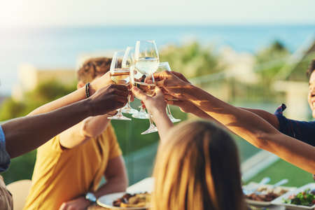 To us growing closer and stronger together. a group of friends raising up their glasses for a toast while sitting around a table together outdoors.の写真素材