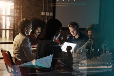 Modern day meetings. a group of young businesspeople sitting around a table and using their digital...