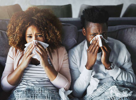 Portrait of a sick couple suffering from the flu, corona or sinus at home together, feeling unwell...