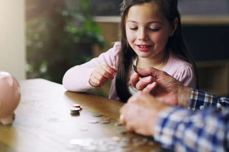 The earlier the better. a little girl learning about money from her grandfather.の写真素材