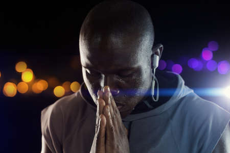 Silent prayers go a long way. Studio shot of a young sportsman holding his hands together in prayer against a dark background.の写真素材