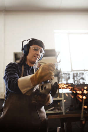 Cutting it to size. an attractive young female artisan using an angle grinder in her workshop.