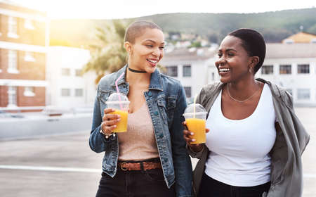 Sharing moments with every sip. two young women walking in the city laughing while holding their cool drinks.の写真素材