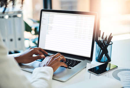 Tech savvy and successful. an unrecognizable woman working on a laptop at her office desk.の写真素材