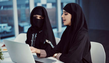 The kind of collaboration great business is made of. two young arabic businesswomen working on a laptop in their office.の写真素材