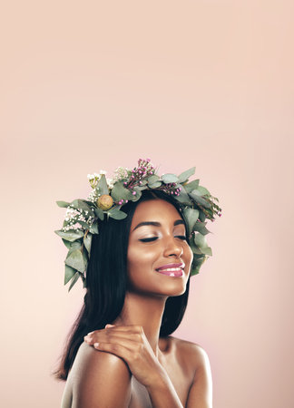 Keeping natures beauty close. Studio shot of a beautiful young woman wearing a wreath while posing with her eyes closed against a pink background.の写真素材