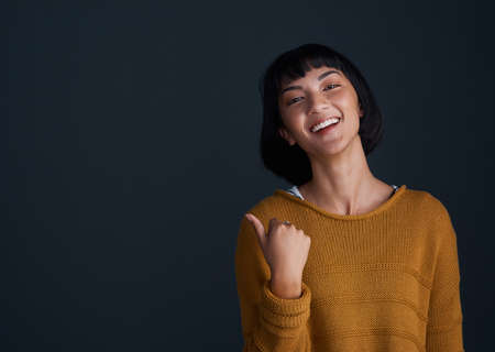 Youll never guess what I found. Studio shot of an attractive young woman pointing against a dark background.の写真素材