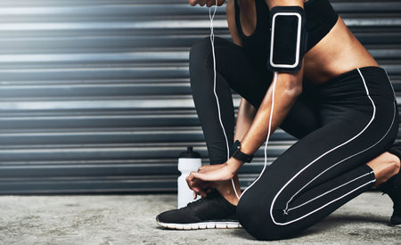 Lets tie these up and get running. Closeup shot of a sporty woman tying her shoelaces while exercising against a grey background.の写真素材